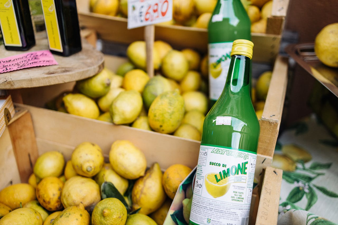 Boxes of fresh lemons with bottles of limone juice at a vibrant market.